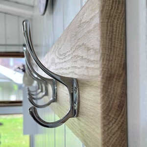 May include: A wooden coat rack with four chrome hooks. The rack is mounted on a white wall.