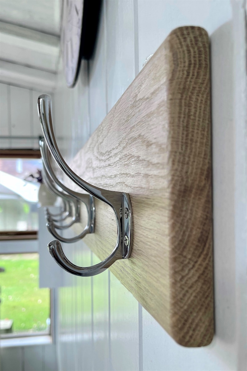 May include: A wooden coat rack with four chrome hooks. The rack is mounted on a white wall.