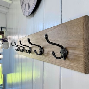 May include: A wooden wall-mounted coat rack with six black metal hooks. The rack is made of natural wood with a light brown finish.