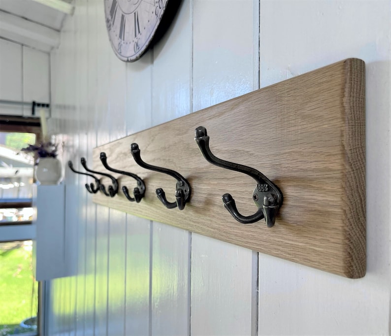 May include: A wooden wall-mounted coat rack with six black metal hooks. The rack is made of natural wood with a light brown finish.