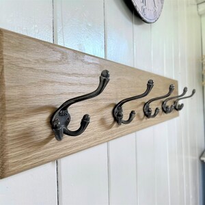 May include: A wooden wall-mounted coat rack with five black metal hooks. The rack is made of light-colored wood and has a natural finish.