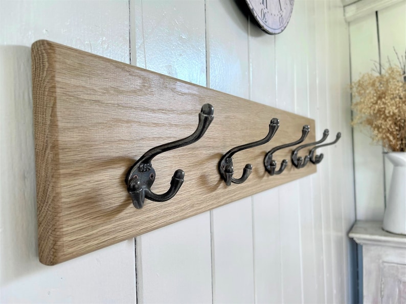 May include: A wooden wall-mounted coat rack with five black metal hooks. The rack is made of light-colored wood and has a natural finish.