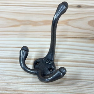 May include: A black metal double hook with a rounded design. The hook has the number "1883" stamped on it.