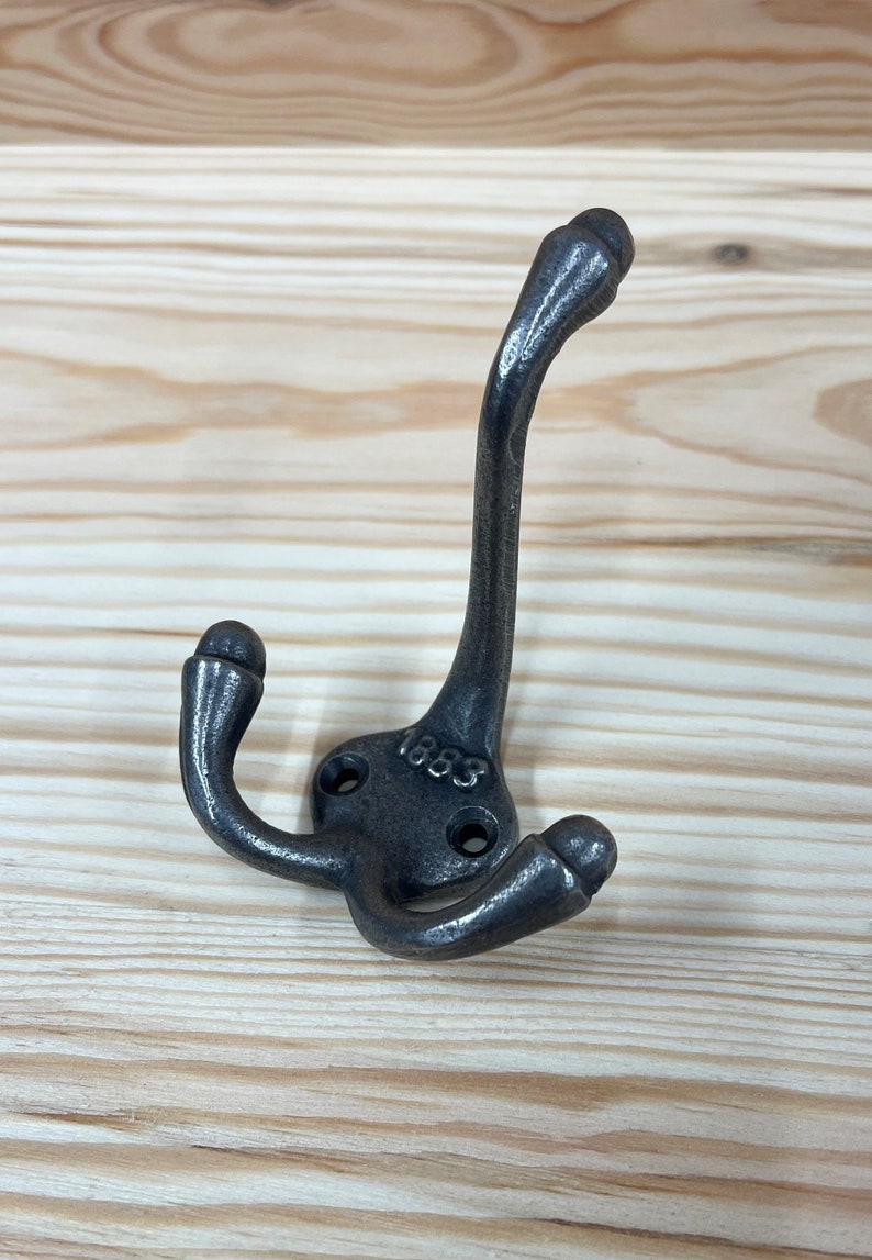 May include: A black metal double hook with a rounded design. The hook has the number "1883" stamped on it.