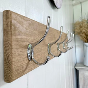 May include: A wooden wall-mounted coat rack with five chrome hooks. The rack is made of light brown wood and has a smooth finish.