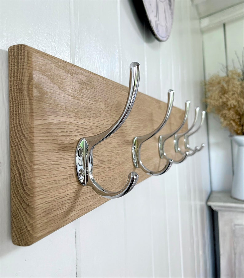 May include: A wooden wall-mounted coat rack with five chrome hooks. The rack is made of light brown wood and has a smooth finish.