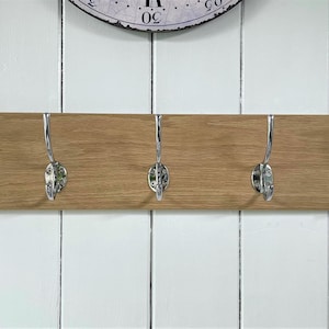 May include: A wooden coat rack with five chrome hooks. The rack is mounted on a white wall.
