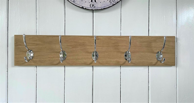May include: A wooden coat rack with five chrome hooks. The rack is mounted on a white wall.