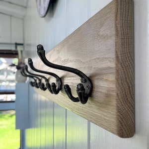May include: A wooden wall-mounted coat rack with six black metal hooks. The rack is made of light brown wood with a natural grain pattern.