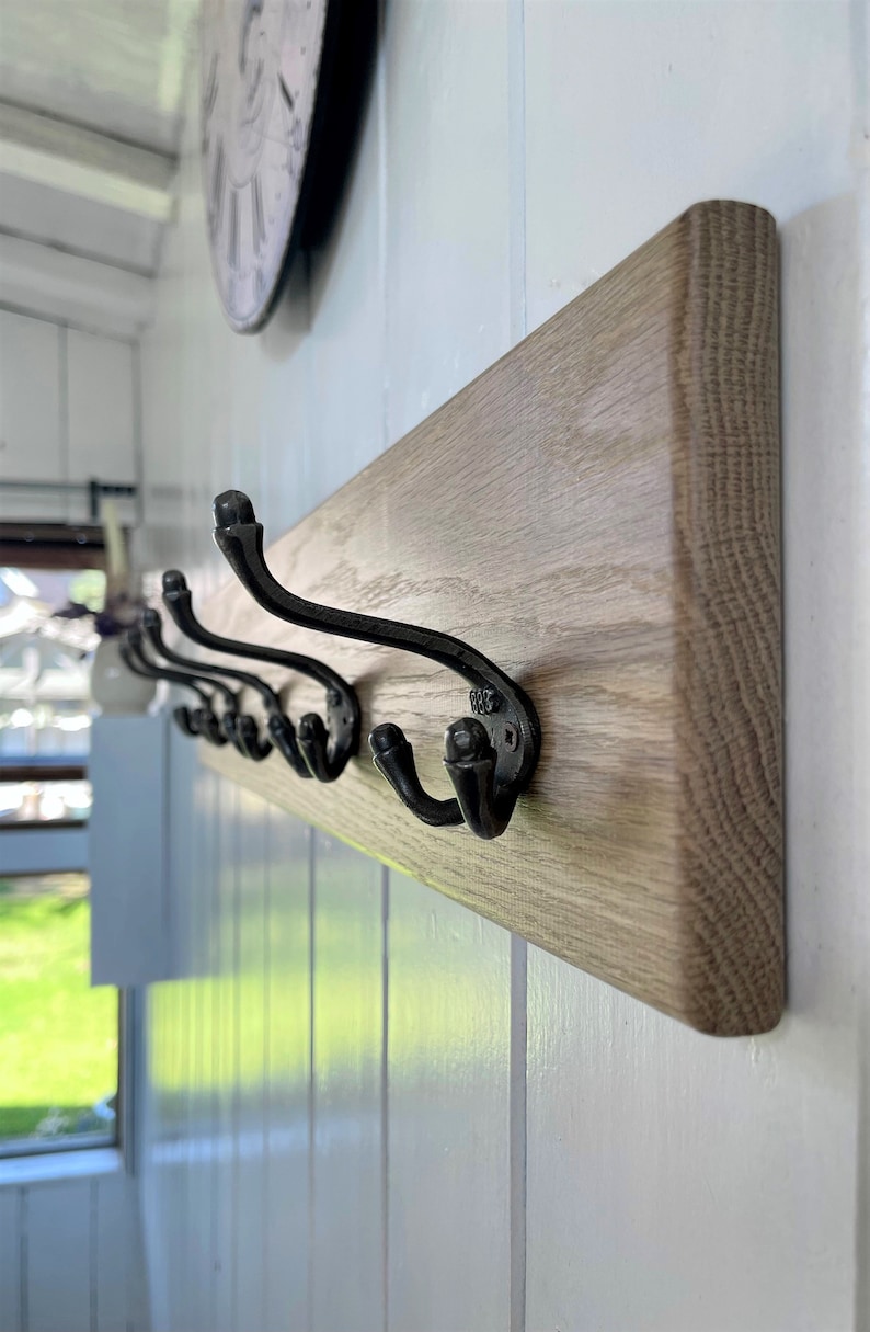May include: A wooden wall-mounted coat rack with six black metal hooks. The rack is made of light brown wood with a natural grain pattern.