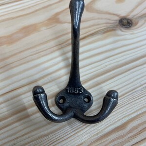 May include: A black metal triple hook with a rounded top and the date "1883" embossed on the base.