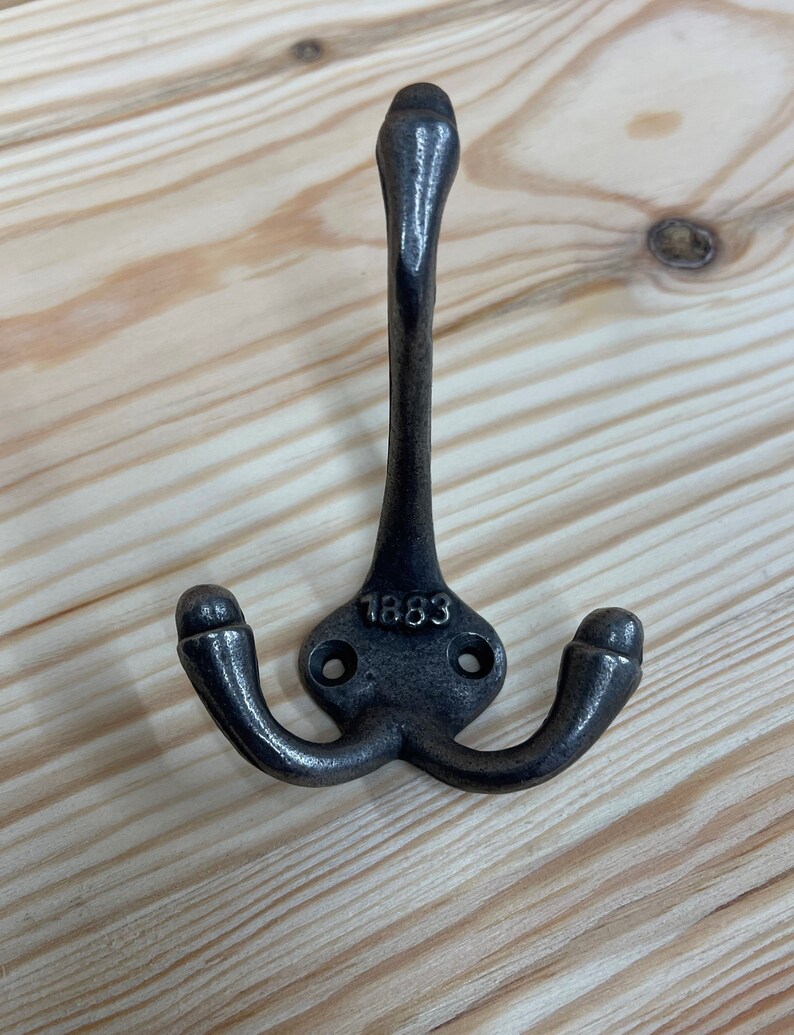 May include: A black metal triple hook with a rounded top and the date "1883" embossed on the base.
