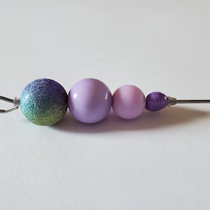 May include: A close-up of a beaded necklace with a silver clasp. The beads are purple, pink, and green with glitter.