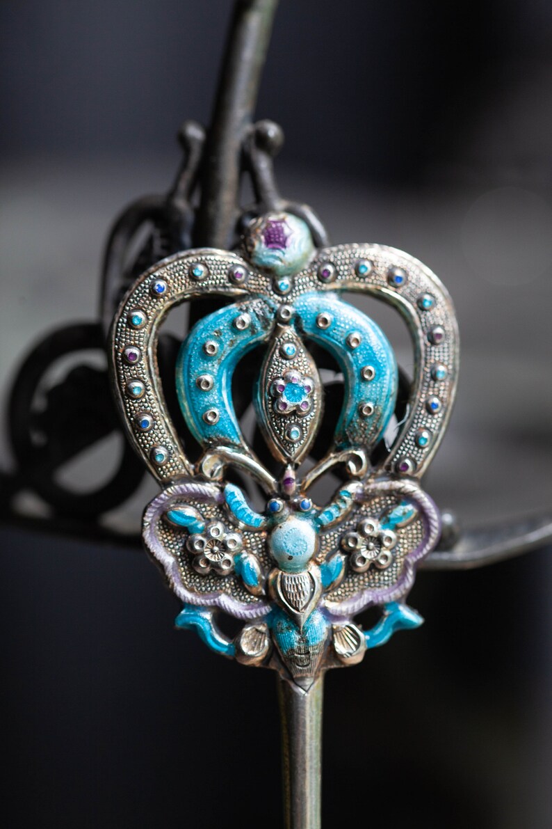 May include: A silver and blue butterfly-shaped hair pin with intricate details and colourful enamel accents.