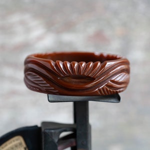 Puede incluir: Un brazalete de plástico marrón tallado con un diseño de sol.