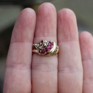 May include: A gold ring with a cluster of pink rubies and smaller diamonds set in a swirl design.