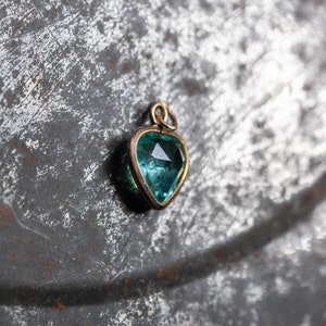 Puede incluir: Un colgante de coraz&oacute;n de oro con una piedra preciosa azul.