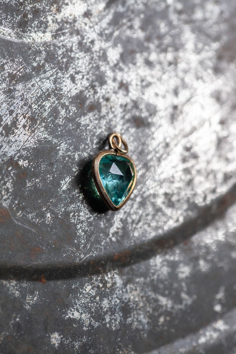 Puede incluir: Un colgante de coraz&oacute;n de oro con una piedra preciosa azul.