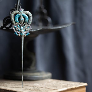 May include: A silver hair stick with a blue and white enamel crown and butterfly design.
