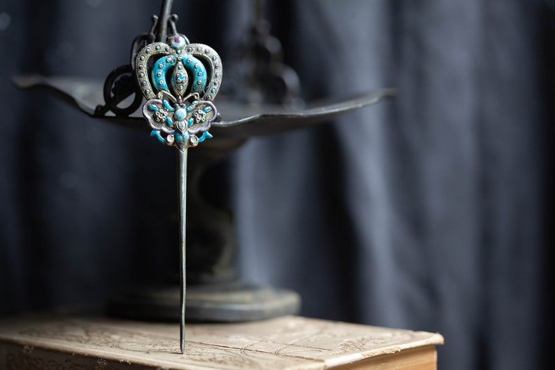 May include: A silver hair stick with a blue and white enamel crown and butterfly design.