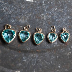 Puede incluir: Cinco colgantes de coraz&oacute;n de oro con detalles de piedras preciosas azules. Los colgantes est&aacute;n dispuestos en fila de mayor a menor.