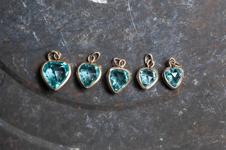 Puede incluir: Cinco colgantes de coraz&oacute;n de oro con detalles de piedras preciosas azules. Los colgantes est&aacute;n dispuestos en fila de mayor a menor.