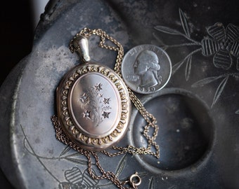 May include: A gold locket with a floral design and small stones on a chain. The locket is sitting on a black surface with a silver quarter next to it.