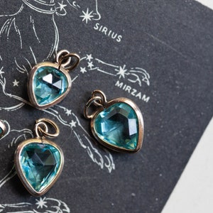 Puede incluir: Cuatro colgantes en forma de coraz&oacute;n con detalles de piedras preciosas azules. Los colgantes est&aacute;n sobre un fondo negro con un mapa de estrellas impreso en &eacute;l. El mapa incluye los nombres Sirius y Mirzam.