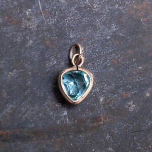 Puede incluir: Un colgante de coraz&oacute;n de oro con una piedra preciosa azul claro.