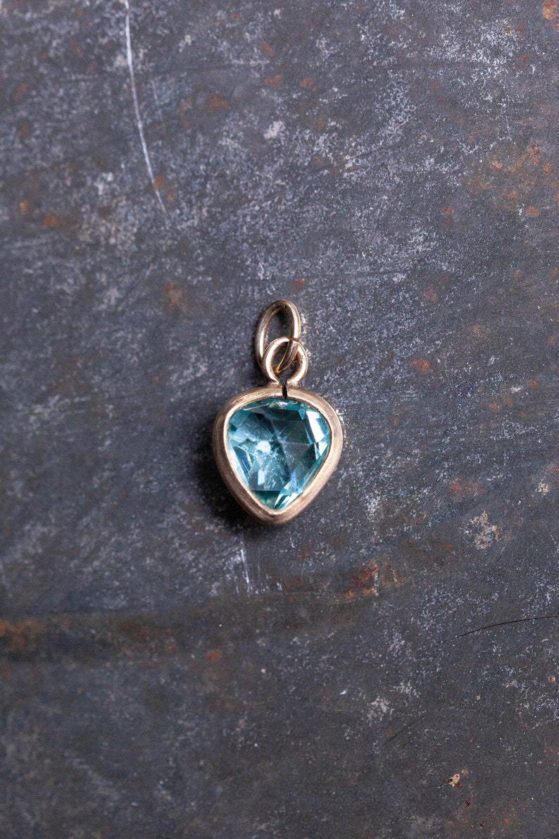 Puede incluir: Un colgante de coraz&oacute;n de oro con una piedra preciosa azul claro.