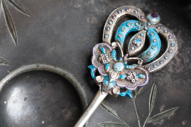 May include: A silver and blue hair ornament with intricate floral designs and a turquoise stone. The ornament is on a dark grey background.