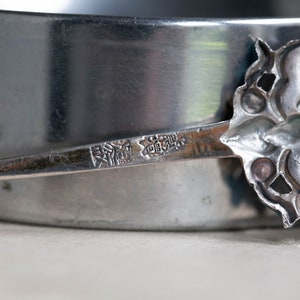 May include: Close-up of a silver spoon with an ornate design. The spoon has a mark on the back that reads "銀製" in Japanese characters.