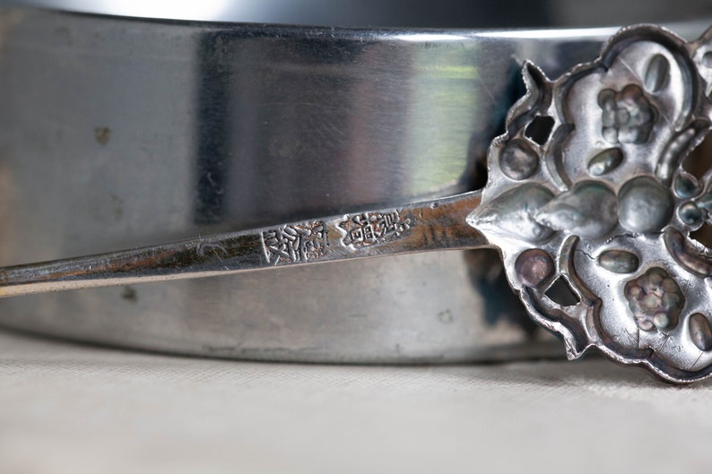 May include: Close-up of a silver spoon with an ornate design. The spoon has a mark on the back that reads "銀製" in Japanese characters.