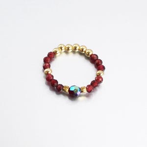 May include: A gold and red beaded ring with a single iridescent blue gemstone in the centre.