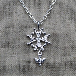 Peut inclure: Collier en argent avec un pendentif en forme de croix et un charme en forme de colombe. La croix est entourée d'un cercle de petites perles.