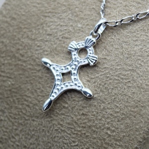 Può includere: Collana con ciondolo in argento con un designo a croce dettagliato e decorato. La croce è testurizzata con piccoli cerchi e ha un'apertura quadrata al centro. Il ciondolo è attaccato a una catena d'argento.