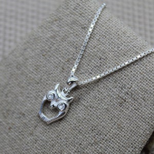May include: A silver chain necklace with an owl pendant. The owl has two small, clear gemstones for eyes.