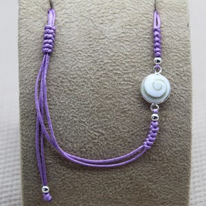 Peut inclure: Un bracelet réglable en cordon violet avec un charme argenté orné d'une coquille d'ormeau blanche et verte.