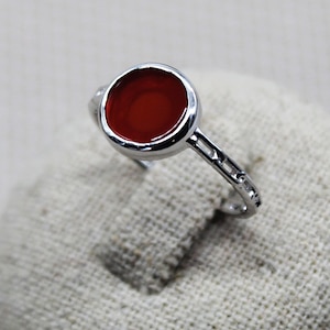 Peut inclure: Une bague en argent avec une pierre de cornaline rouge sertie dans un sertissage à bélière.
