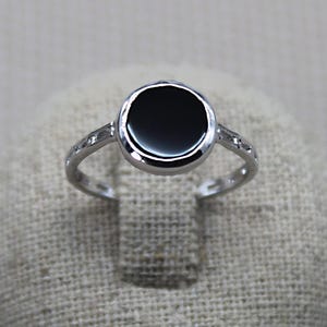 May include: A silver ring with a black stone set in a round bezel. The ring has a simple band with small accents.