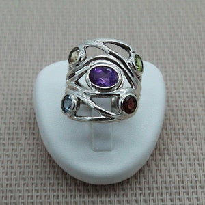 Puede incluir: Anillo de plata con un diseño retorcido y cinco piedras preciosas: amatista, verde, azul, marrón y rojo.