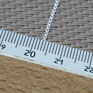 May include: A close-up of a silver chain measured against a ruler. The chain is 20 inches long.