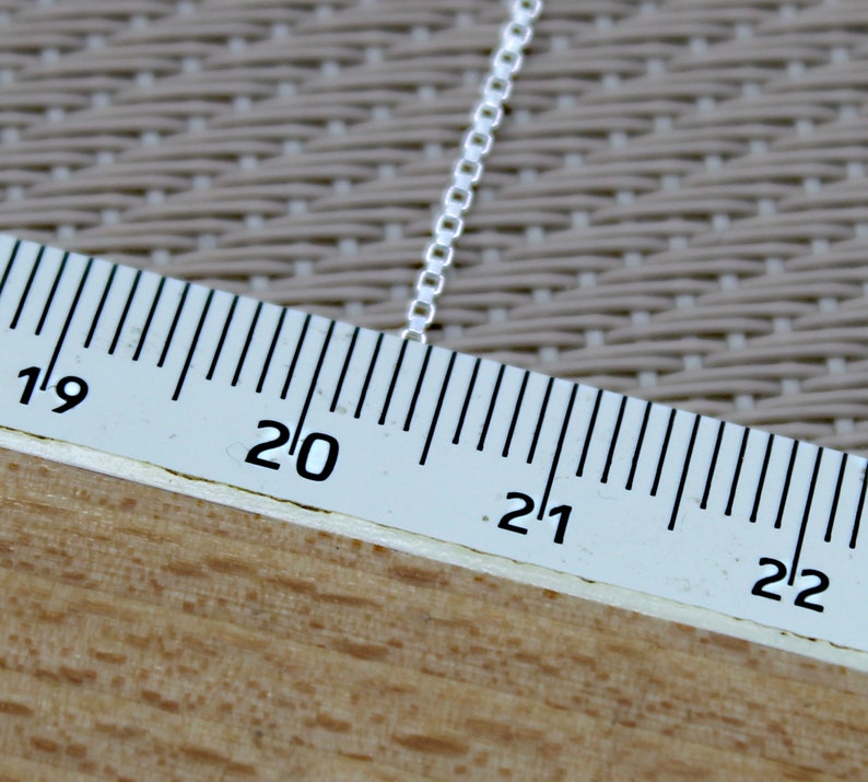 May include: A close-up of a silver chain measured against a ruler. The chain is 20 inches long.
