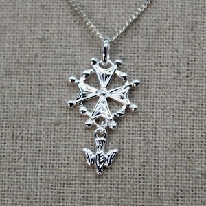 Peut inclure: Collier avec pendentif en argent représentant une croix avec un charme de colombe. La croix est entourée d'un cercle de petites perles.