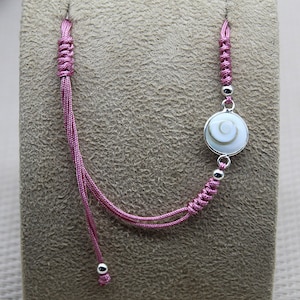 Peut inclure: Un bracelet réglable en cordon rose avec un charme argenté en forme de coquille blanche et grise.