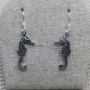 Può includere: Un paio di orecchini pendenti in argento con un design dettagliato di cavalluccio marino. I cavallucci marini sono testurizzati e hanno una finitura leggermente ossidata.