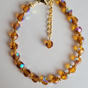 May include: A gold-toned bracelet featuring faceted amber-colored beads with iridescent highlights. The bracelet has a gold chain extender and clasp. The beads are strung together with small gold-colored beads.
