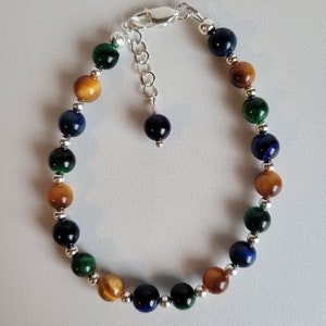 May include: A beaded bracelet with alternating tiger's eye, blue, and green stones. The bracelet has a silver clasp and a silver charm.