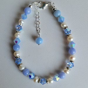 May include: A delicate bracelet featuring a mix of light blue and white beads. The bracelet has a silver clasp and a small light blue bead charm.