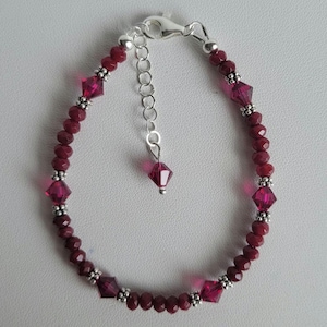 May include: A bracelet featuring deep red faceted crystal beads interspersed with small silver-toned metal spacer beads. The piece includes a silver-toned lobster claw clasp, an adjustable chain extender, and a single dangling crystal bead charm.